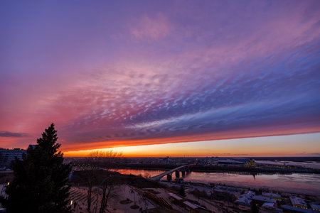 A mesmerizing sunset over Strelka in Nizhny Novgorod, featuring Kanavinsky Bridge. The frozen river and glowing city lights create a stunning winter viewの写真素材