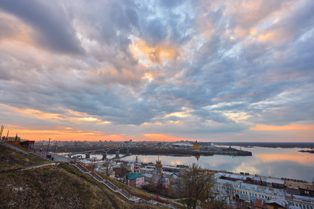 A breathtaking sunset over Strelka in Nizhny Novgorod, featuring the Oka River, Kanavinsky Bridge, Rozhdestvenskaya Church, and Alexander Nevsky Cathedral against a vibrant skyの写真素材