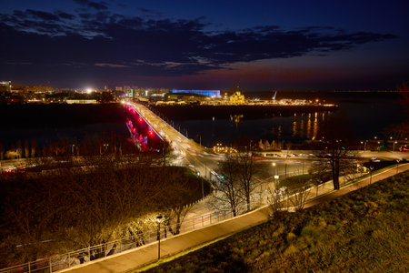 Stunning view of Kanavinsky Bridge and Alexander Nevsky Cathedral in Nizhny Novgorod at dusk, glowing city lights reflected in the icy river beneath a vibrant night skyの写真素材