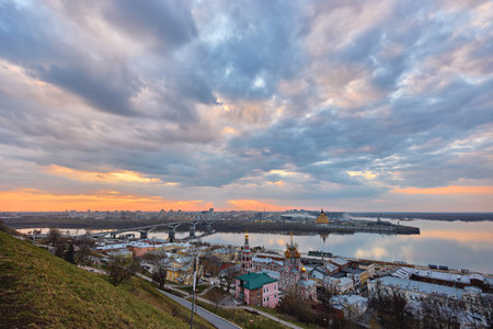 A breathtaking sunset over Strelka in Nizhny Novgorod, featuring the Oka River, Kanavinsky Bridge, Rozhdestvenskaya Church, and Alexander Nevsky Cathedral against a vibrant skyの写真素材