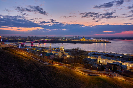 A magical twilight view of Strelka in Nizhny Novgorod, showcasing the lit-up Kanavinsky Bridge, Rozhdestvenskaya Church, and Alexander Nevsky Cathedral reflecting on the Oka Riverの写真素材