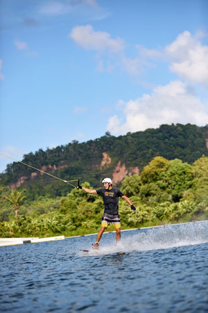 Young man wakeboarding on a lake, wearing helmet and gloves, riding smoothly with a splash trailの写真素材