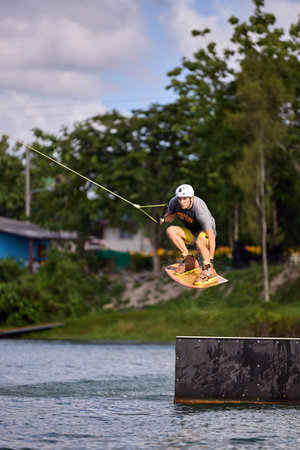 Skilled wakeboarder in mid-air performing a trick over an obstacle. Extreme sport action on waterの写真素材