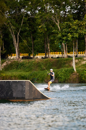 Young man wakeboarding on a lake, wearing helmet and gloves, riding smoothly with a splash trailの写真素材