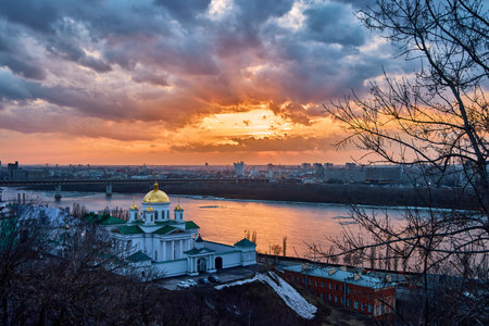 A breathtaking winter sunset over the Annunciation Monastery in Nizhny Novgorod, Russia. The golden domes contrast beautifully against the dramatic sky and the shimmering riverの写真素材