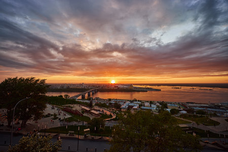 A mesmerizing sunset over Strelka in Nizhny Novgorod, featuring Kanavinsky Bridge and the illuminated Alexander Nevsky Cathedral. The frozen river and glowing city lights create a stunning winter viewの写真素材