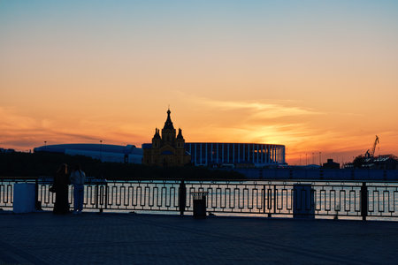 Silhouette of two women by a fence on the embankment, facing Alexander Nevsky Cathedral and a stadium on Strelka at sunsetの写真素材