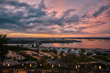 A mesmerizing sunset over Strelka in Nizhny Novgorod, featuring Kanavinsky Bridge and the illuminated Alexander Nevsky Cathedral. The frozen river and glowing city lights create a stunning winter viewの写真素材