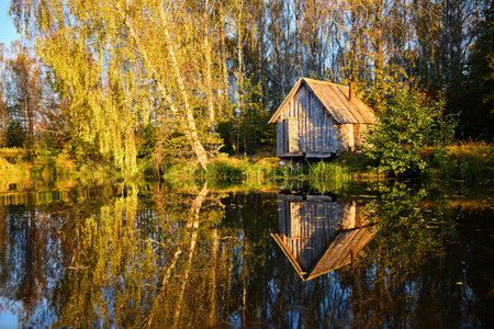 A serene riverside scene with a wooden house and lush trees, perfectly reflected in the calm waterの写真素材