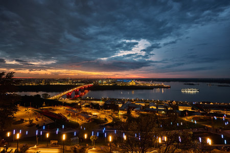 Stunning view of Kanavinsky Bridge and Alexander Nevsky Cathedral in Nizhny Novgorod at dusk, glowing city lights reflected in the icy river beneath a vibrant night skyの写真素材