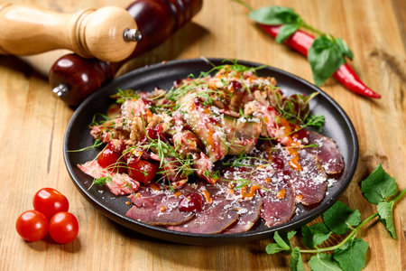 Gourmet salad with tender dried lamb, raspberry-chili sauce, cherry tomatoes, greens, herbs, and grated cheeseâserved on a black plate for bold visual appealの写真素材