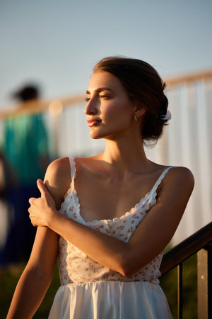 Slavic girl in white floral lace dress stands in golden sunlight, creating a serene, dreamy moodの写真素材