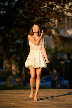 Slavic girl in light summer dress walks along a wooden path during golden hour in the parkの写真素材