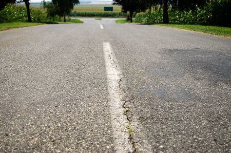 Road white line on asphalt close up with green grass aside