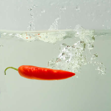 hot pepper falling in water on white background