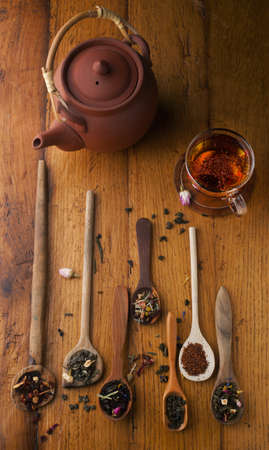 Cup of tea and teapot and assorted herbs and tea with a spoon on a wooden backgroundの写真素材
