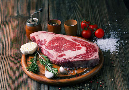 Raw ribeye steak marbled meat with salt, rosemary and garlic on a wooden backgroundの写真素材