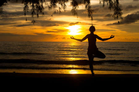 A woman practicing yoga on beach at sunset の写真素材