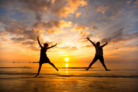 Young couple in a jump on the sea beach at sunsetの写真素材