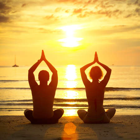 Young couple practicing yoga on the beach at sunsetの写真素材