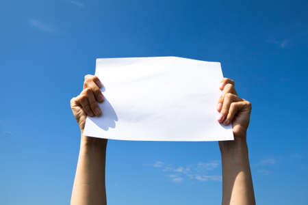 Hands holding clean white sheet paper over the sky の写真素材