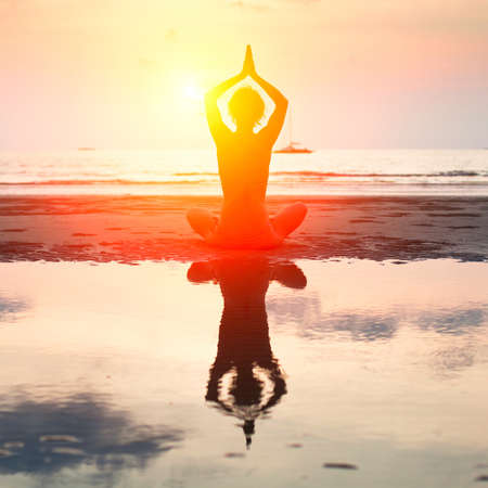 Silhouette of a beautiful yoga woman on the beach at sunset の写真素材