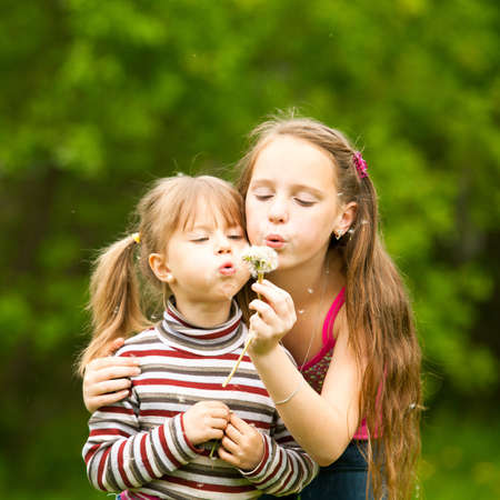 Cute 5 year old and 11 year old girls blowing dandelion seeds away.の写真素材