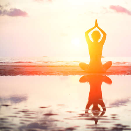 Yoga woman sitting in lotus pose on the beach during sunset, with reflection in water  in bright colors の写真素材