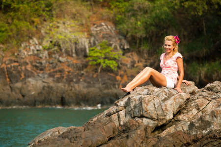 Beautiful blonde girl is sitting on the rocks at the seaside の写真素材
