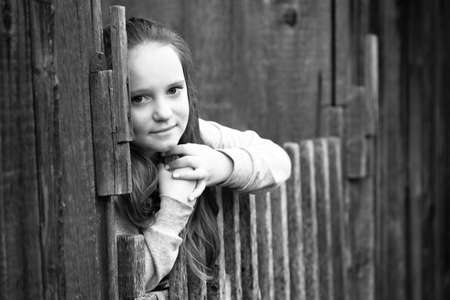 Portrait of teen-girl standing near vintage rural fence, black-and-white photo.の写真素材