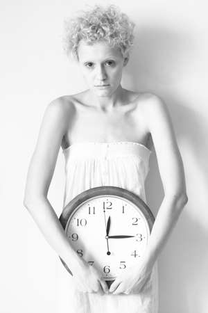Scrawny girl with big clock in hands, black and white photo.の写真素材