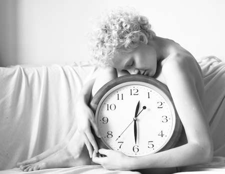 Conceptual portrait of woman in bed with big clock, black and white photo.