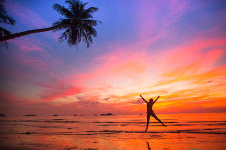 Young girl in a jump on the sea beach at sunset (concept of long-awaited vacation)の写真素材