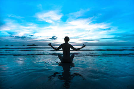 Sunset yoga woman on sea coast (in cold colors)の写真素材