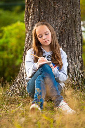 Teen-girl writing in a notebook while sitting in the parkの写真素材