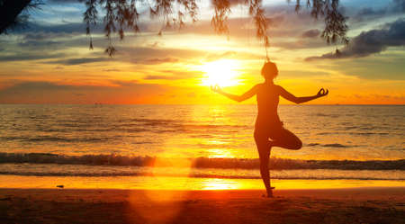 Young woman practicing yoga by the sea at sunsetの写真素材