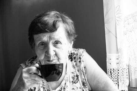 Portrait an old woman is drinking tea, black and white.の写真素材