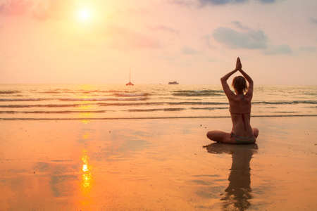 Silhouette young woman practicing yoga on the sea beach at sunset.の写真素材