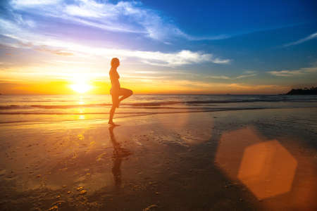 Silhouette of a young woman doing exercises at sunset on the seashore.の写真素材