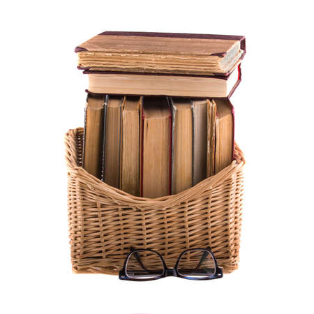 Stack of old antique books in a wicker basket and spectacles in thick-rimmed, isolated on white background.の写真素材