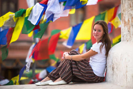 Young girl sitting on Buddhist stupa, prayer flags flying in the background.の写真素材