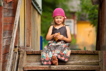 Beautiful little five-year girl on the porch of a village houseの写真素材