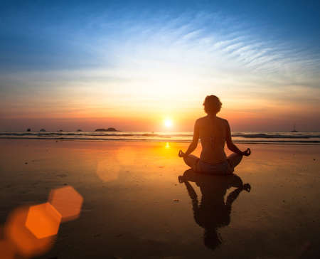 Woman meditating on the beach at sunset.の写真素材