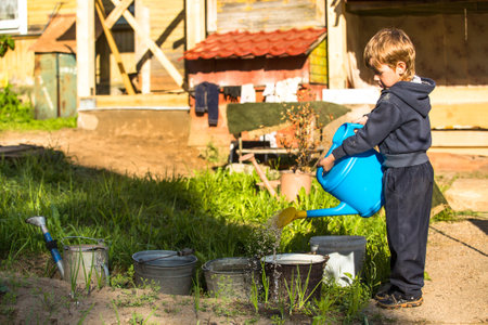 Little boy watering a flower bed near the village house.のeditorial素材