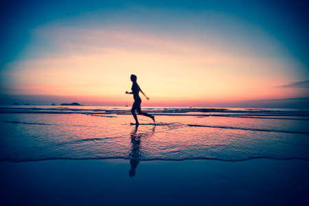 Blured silhouette of a woman jogger on the beach at sunset, surreal colours.の写真素材