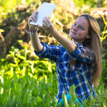 Nice teengirl in nature and taking selfie on a tablet PC の写真素材