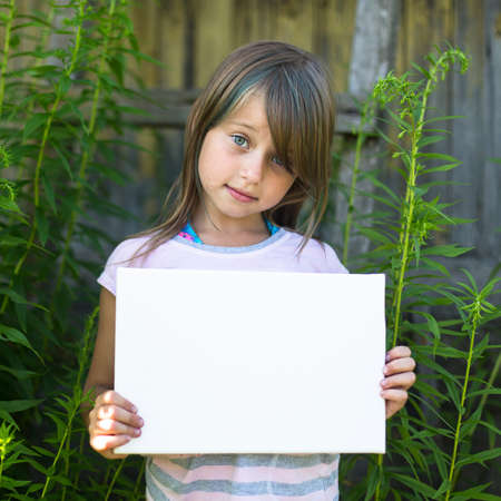 Cute little girl holding clean white sheet paper, outdoors (banner is for your message)