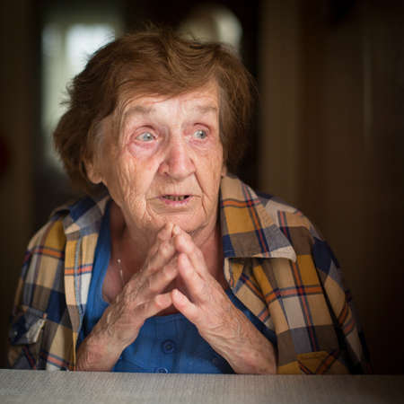 Close-up shot of old woman sitting at table in his house.