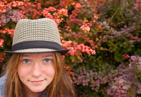 Portrait of cute young girl wearing a hat in the lush garden.