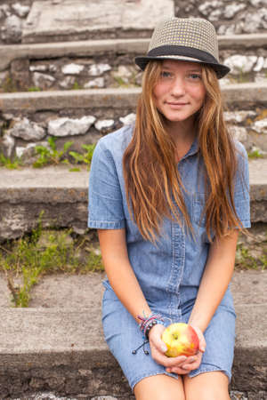Beautiful young girl sitting in the park, with an apple in his hand.の写真素材